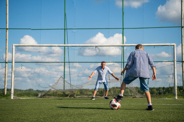 Chico pateando un penal en el gol jugando con su padre en una hierba verde
. - Foto, Imagen