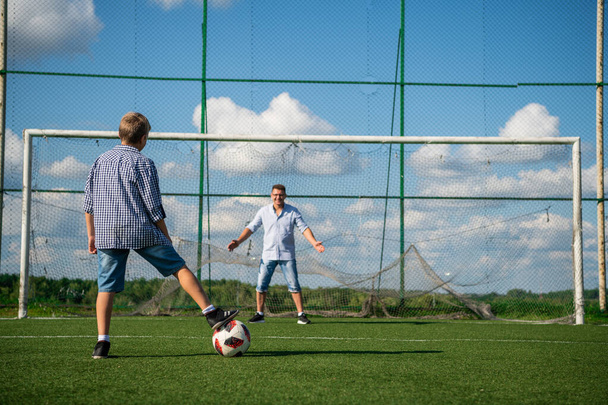 Szczęśliwy ojciec i podekscytowany syn grający razem w piłkę na zielonym boisku do piłki nożnej biegający po trawie kopiący piłkę. Tata i chłopak związek i zdrowy styl życia. - Zdjęcie, obraz