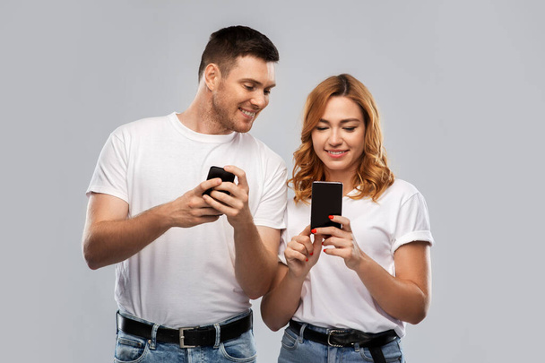 happy couple in white t-shirts with smartphones - Φωτογραφία, εικόνα