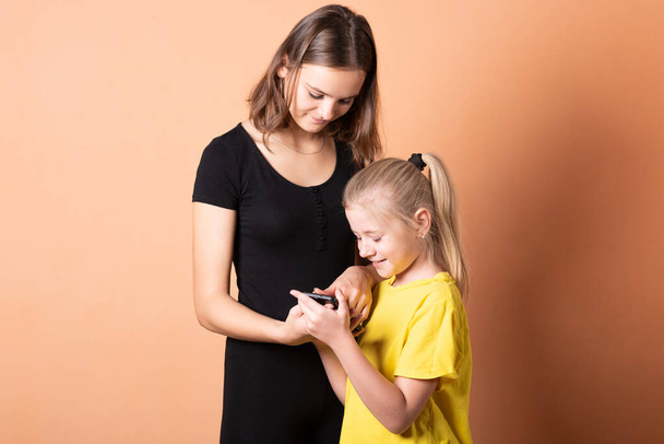 La hermana le pide a su hermana un smartphone. sobre un fondo naranja claro
. - Foto, imagen