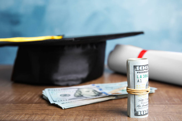 Dollar banknotes and student graduation hat on wooden table against blue background. Tuition fees concept - Foto, Imagem