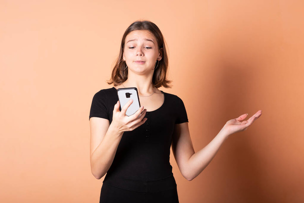 Дівчина показує невдоволення зі смартфоном на світло-оранжевому фоні
. - Фото, зображення