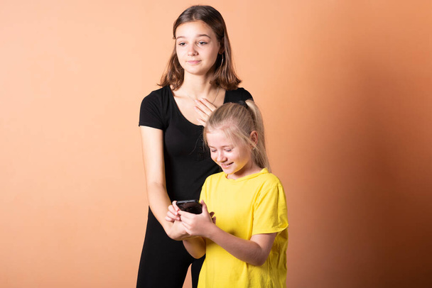 Zwei Schwestern teilen sich ein Smartphone. auf hellorangefarbenem Hintergrund. - Foto, Bild