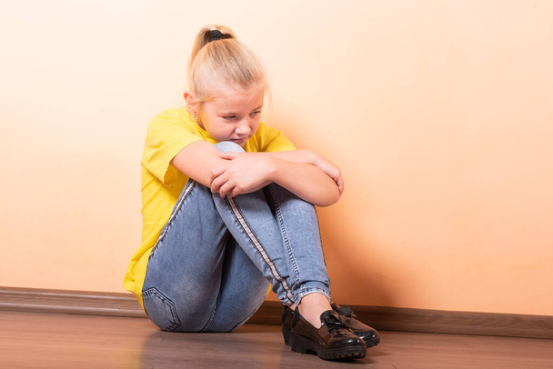 Meisje zit beledigd op de vloer, licht oranje achtergrond. - Foto, afbeelding
