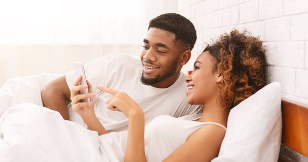 glücklich liebendes schwarzes Paar vernetzt sich auf Mobiltelefonen im Bett - Foto, Bild