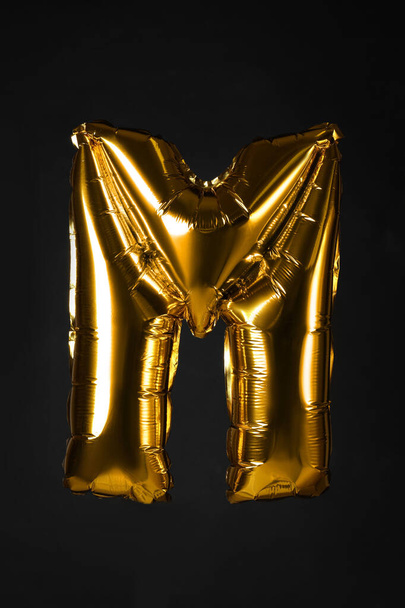 Golden letter M balloon on black background - Foto, imagen