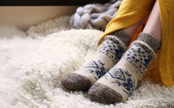 Woman wearing knitted socks on window sill indoors, closeup. Warm clothes - Фото, изображение