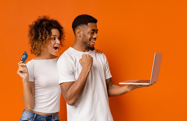 Homme et femme africains joyeux avec carte de crédit travaillant sur ordinateur portable
 - Photo, image