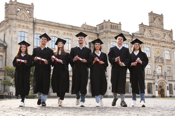 Счастливые студенты с дипломами на открытом воздухе. Выпускная церемония
 - Фото, изображение