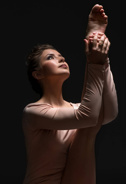 Woman in beige body streching leg in dark studio - Fotó, kép