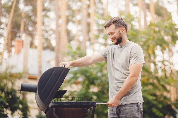 Homem frita carne na churrasqueira no jardim da natureza
 - Foto, Imagem