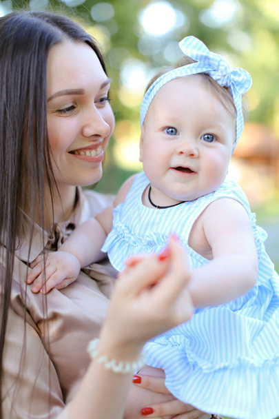 Zbliżenie szczęśliwy uśmiechający się matka trzyma dziecko mało kobiet w niebieskiej sukience. - Zdjęcie, obraz