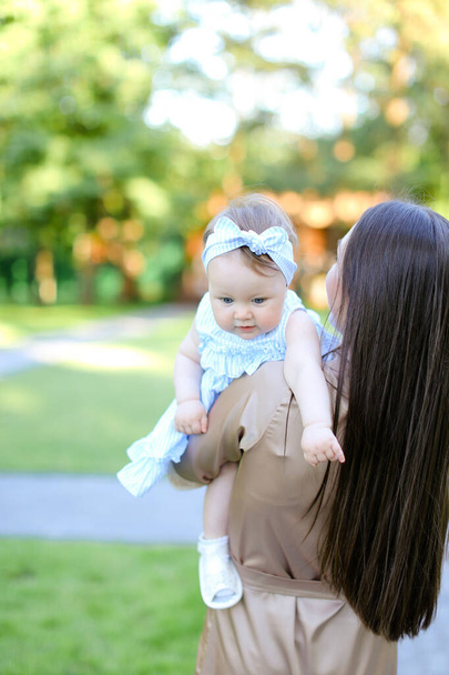 Back view of young brunette woman holding little baby in garden. - Foto, Imagem
