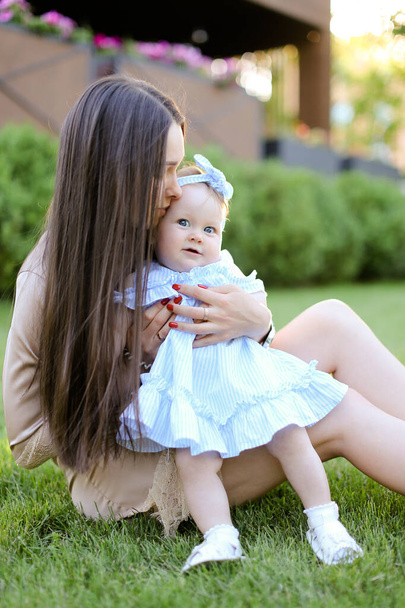 junge Mutter mit langen Haaren sitzt mit kleiner Tochter im Gras. - Foto, Bild