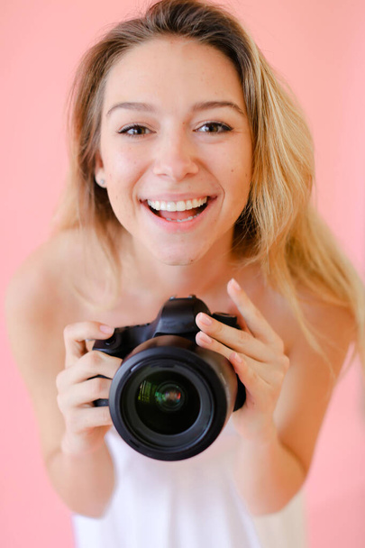 Closeup young happy female photographer with camera in pink monophonic background. - Photo, Image
