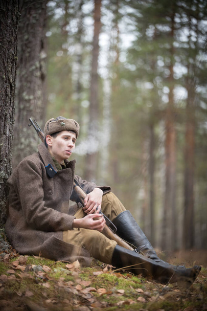 Um soldado da Segunda Guerra Mundial em roupas militares está sentado na floresta e fumando
 - Foto, Imagem
