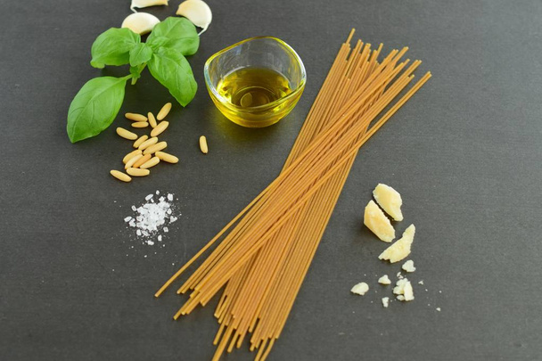 Italiaanse keuken met volkoren pasta en pesto ingrediënten; basilicum, knoflook, olijfolie, pijnboompitten, parmezaanse kaas en zout. Zwarte achtergrond - Foto, afbeelding