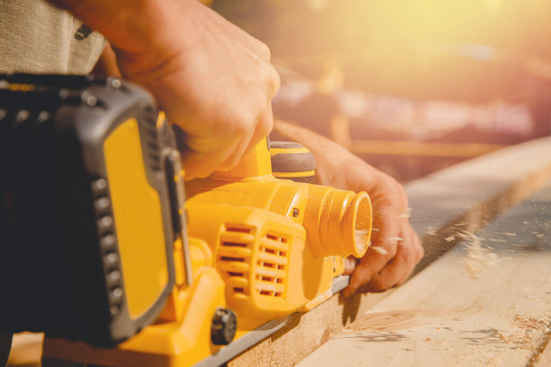 Homme mains travailleur tenir raboteuse électrique de travail avec planche en bois, la poussière lisse
 - Photo, image