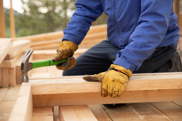 Constructor masculino en guantes amarillos clavo de martillo en la estructura de madera. Concepto de construcción
 - Foto, Imagen