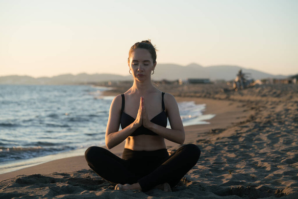 Young caucasian woman practicing yoga on the beach near calm sea - Photo, Image
