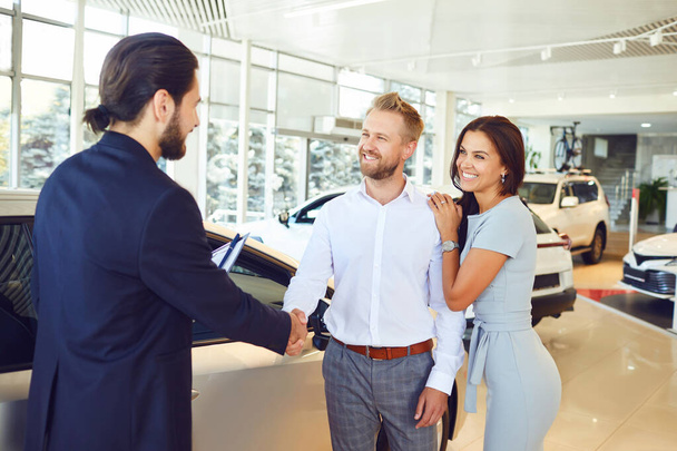 A car salesman and a buyer shake hands. A couple buys a car - Фото, изображение
