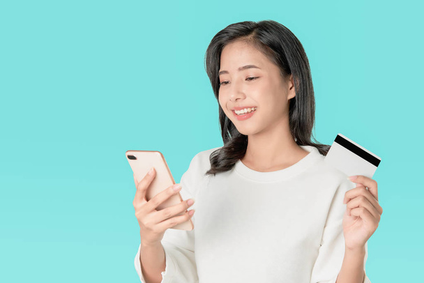 Улыбайтесь счастливо азиатские женщины белые футболки держа смартфон и кредитные карты покупки в Интернете на синем фоне
. - Фото, изображение