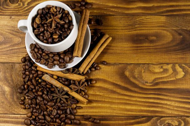 Coffee beans in white cup, star anise and cinnamon sticks on wooden table. Top view, copy space - Φωτογραφία, εικόνα