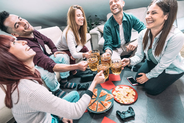 Young millenial friends eating pizza at home after college - Friendship concept with roomates students enjoying time together having fun at shared apartment with tech devices and videogame controllers - Photo, Image