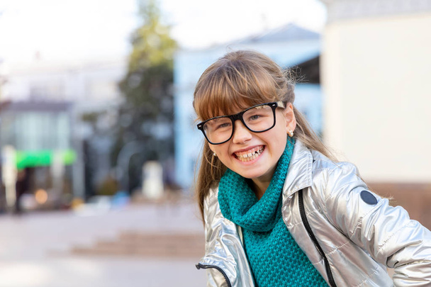 Cheerful girl of 9 - 10 years in glasses against the background of the city. Happy child. - Photo, Image