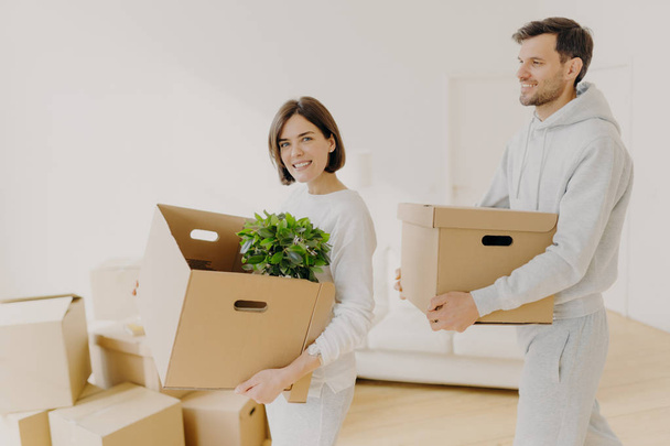 Photo of family couple carry big boxes with households items and personal belongings, move into new home, enter new bought or rented house. Happy homeowners busy with unpacking. Domestic routine - Photo, Image