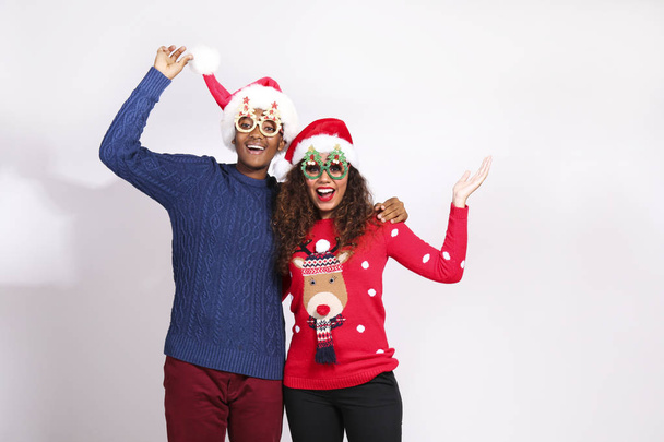 Studio portrait of young couple, boyfriend & girlfriend with dark skin wearing santa claus hat and christmas outfit. Ugly sweater concept. Close up, copy space for text, isolated background. - Foto, afbeelding