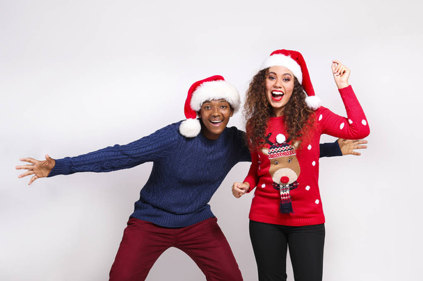Studio portrait of young couple, boyfriend & girlfriend with dark skin wearing santa claus hat and christmas outfit. Ugly sweater concept. Close up, copy space for text, isolated background. - Fotó, kép