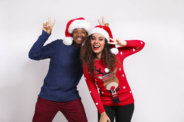 Studio portrait of young couple, boyfriend & girlfriend with dark skin wearing santa claus hat and christmas outfit. Ugly sweater concept. Close up, copy space for text, isolated background. - Valokuva, kuva