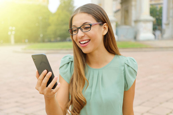 Sorridente giovane donna d'affari con gli occhiali facendo videochiamata con il suo smart phone all'aperto
. - Foto, immagini