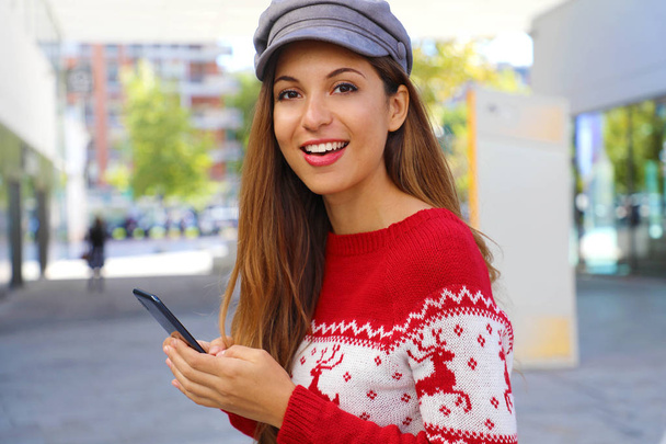 Χριστουγεννιάτικη μόδα γυναίκα αγοράζουν σε απευθείας σύνδεση στο έξυπνο τηλέφωνο στο εμπορικό κέντρο. - Φωτογραφία, εικόνα