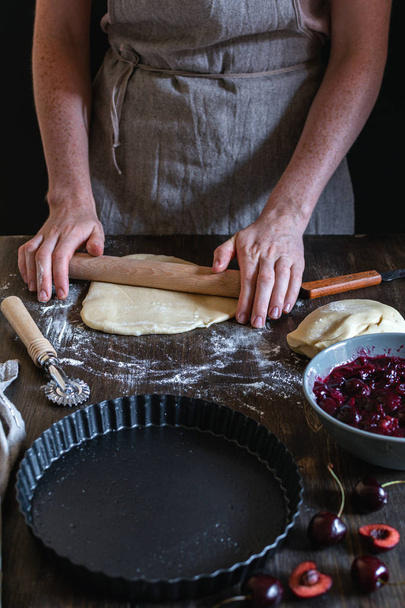Mani femminili che cucinano torta di ciliegie con ingredienti su legno rustico
 - Foto, immagini