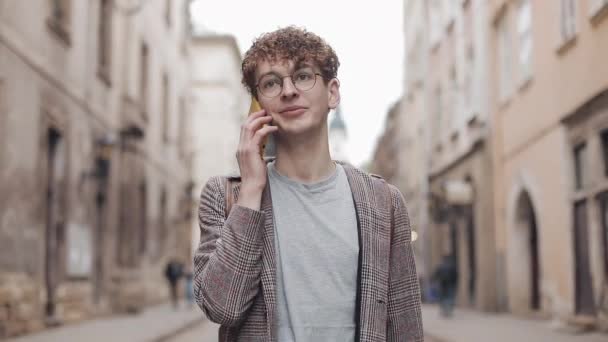 Young Hipster Guy in Glasses Wearing Checked Jacket, Talking, Chatting on the Smartphone, Smiling, Walking at Old City Background. Communication, Student, Tourist Concept. Urban Lifestyle. - Video, Çekim