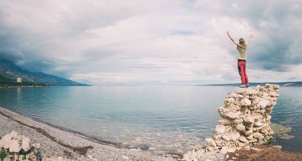 Дівчина стоїть на купі каменів і дивиться на море
. - Фото, зображення