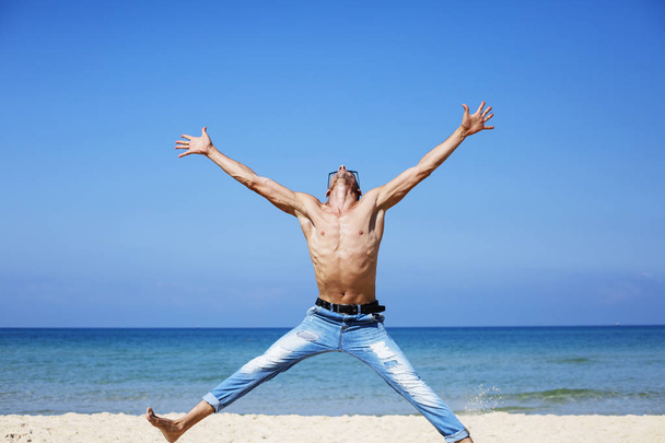 young muscular man resting and posing on the beach. Jump in the air - Photo, image