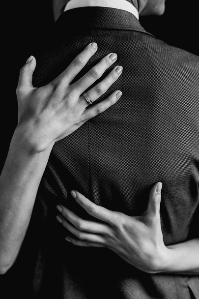 bride hugs the groom in a jacket with two hands in black and white - Fotografie, Obrázek