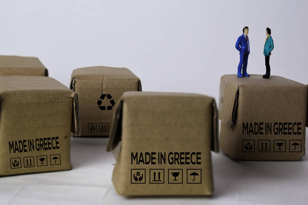 Miniaturowy biznesmen Mówienie na pudełkach z tekstem Made In Greece odizolowany biały piekarnia - Zdjęcie, obraz