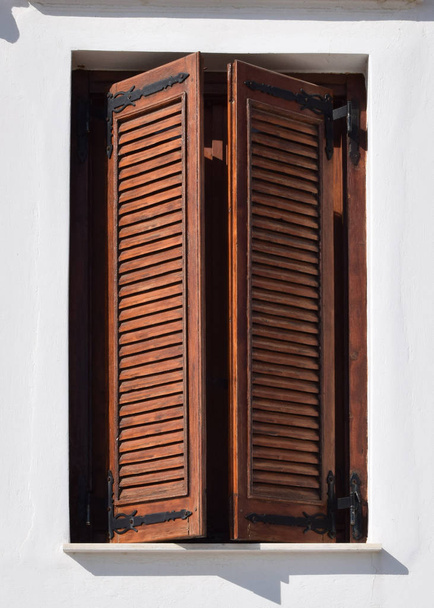 egy mediterrán ház fából készült ablaktáblái. fehér fal, barna redőnyökkel lezárt ablakkal. - Fotó, kép