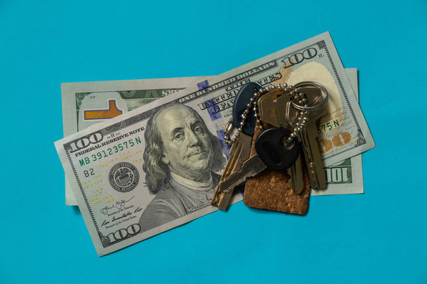 ключи от квартиры лежат на банкноте за 100 долларов на синем фоне крупным планом
 - Фото, изображение