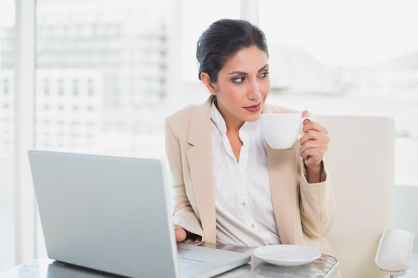 Thinking businesswoman holding cup while working on laptop - Foto, immagini