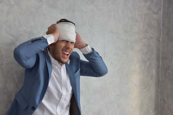 Overworked businessman with bandaged hurt head at workplace with scattered documents - Photo, Image