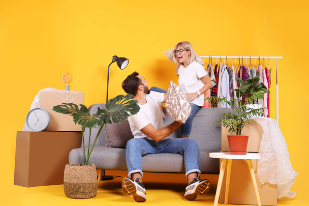 Young couple in matching outfits having fun moving boxes, isolated on yellow. - Фото, изображение