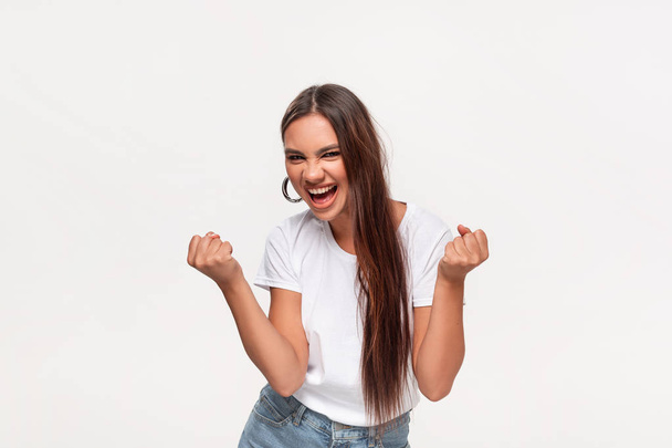 Excited african-american teenager in a white t-shirt and blue jeans dancing isolated over white background. Concept of success - Photo, Image