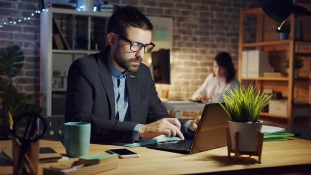 Handsome businessman getting good news on laptop working in office in evening - Footage, Video