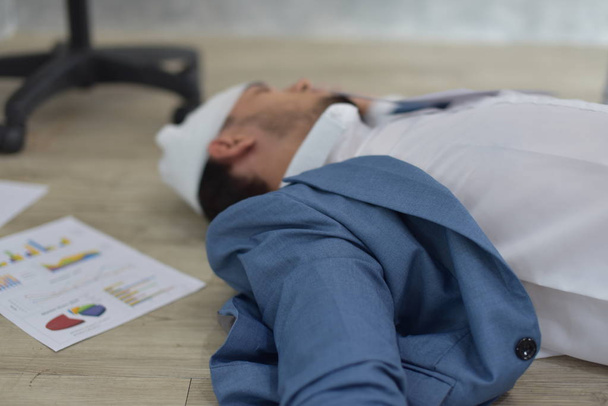 雑然とした文書で床に横たわっている包帯を傷つけた頭を持つ過労のビジネスマン - 写真・画像