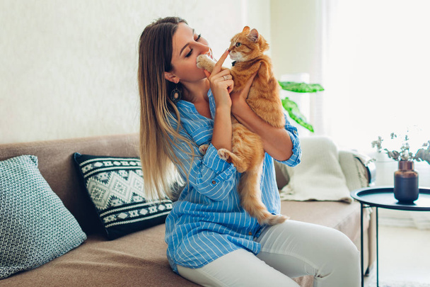 Bawię się z kotem w domu. Młoda kobieta siedzi na kanapie drażniąc i przytulając zwierzaka. - Zdjęcie, obraz